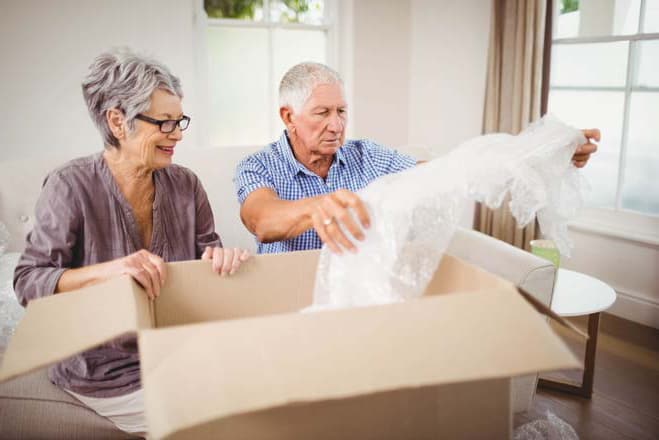 gray-haired couple with a moving box as they work on downsizing to an adult retirement community