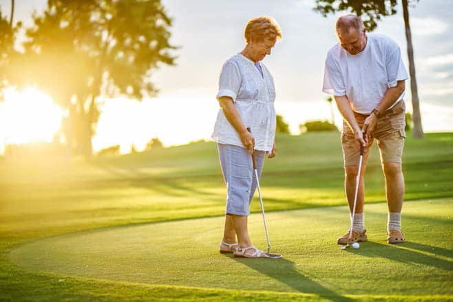 older couple playing golf in the sunset at their 55 and over residential community